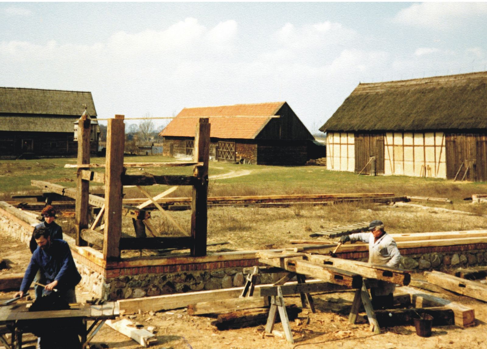 Trzech praconików muzeum podczas budowy stodoły. Widoczne fundamenty i drewniane pale.